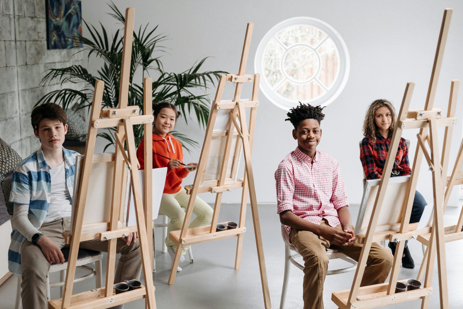Teens drawing in a bright art classroom, seated at easels, engaged in creativity.